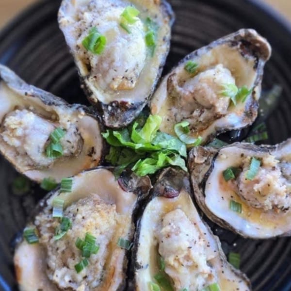 Six baked oysters topped with cheese, black pepper, and green onions on a black plate.