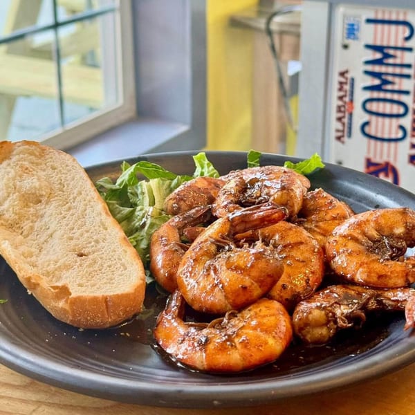 A plate of BBQ shrimp with a side of bread and lettuce, with an Alabama license plate in the background.