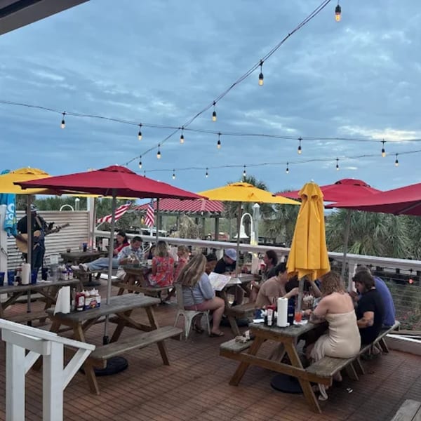 Patrons enjoying outdoor dining at Sunny Daze Smokehouse with live music under string lights and umbrellas.